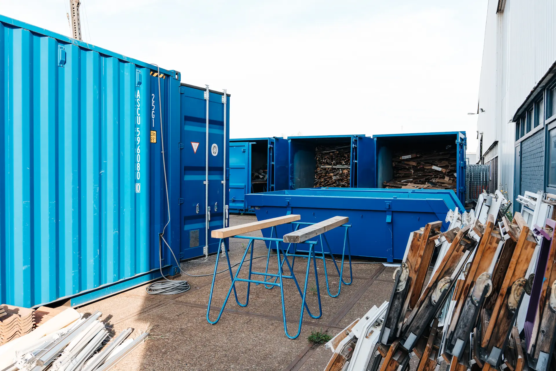 Recyclingcontainers met oude kozijnen op de werkplaats